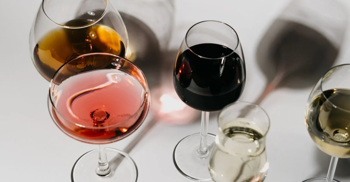 Une variété de verres à vin sur une surface blanche propre, présentant différents types et couleurs de vin.