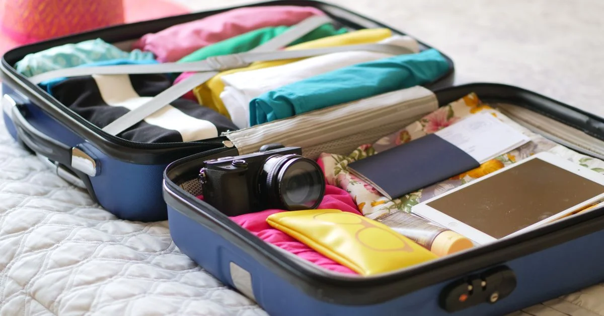 Valise ouverte avec appareil photo, vêtements et passeport, prête pour des vacances d'été.